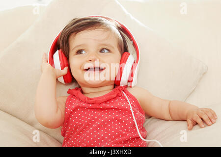 Babymädchen auf Sofa rot Kopfhörer anhören Stockfoto