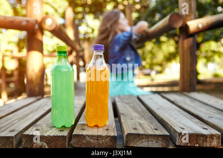 Junges Mädchen lehnte sich auf Klettergerüst im Park, zwei Mineralwasser alkoholfreie Getränke im Vordergrund Stockfoto