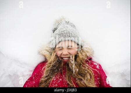 Mädchen auf Rücken im Schnee liegend mit Augen geschlossen Stockfoto