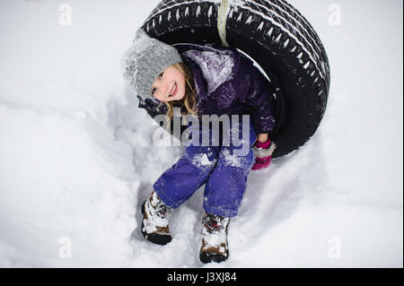 Obenliegende Porträt eines Mädchens auf Reifenschaukel im Schnee Stockfoto