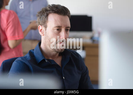 Mann am Computer im Büro arbeiten, Kollegen auf Kaffeepause im Hintergrund Stockfoto