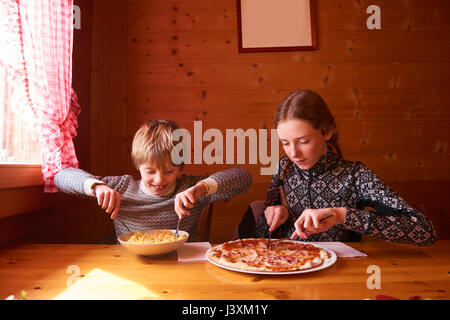Jugendmädchen und Bruder essen Pasta und Pizza im Chalet Tabelle Stockfoto