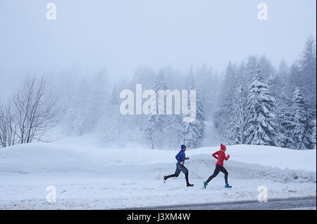 Fernsicht auf weibliche und männliche Läufer in tiefem Schnee läuft, Gstaad, Schweiz Stockfoto