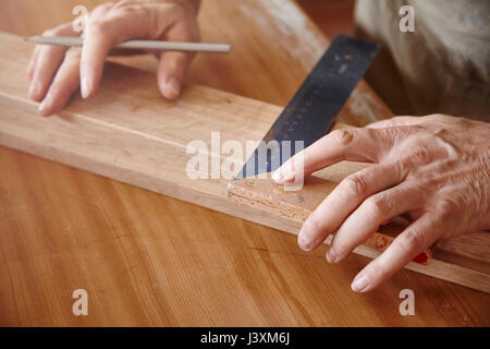 Die Hände der männlichen Tischler mit Quadrat in der Workbench Stockfoto