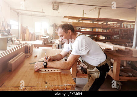 Männliche Tischler Kennzeichnung Holz mit Bleistift an der Werkbank Stockfoto