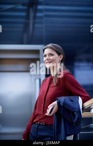 Geschäftsfrau, lehnend auf Office Handlauf holding Smartphone Stockfoto