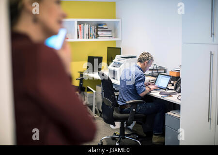 Mann an Schreibtisch im Büro mit Laptops Stockfoto