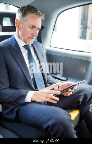 Reifen Geschäftsmann am digitalen Tablette im Taxi suchen Stockfoto