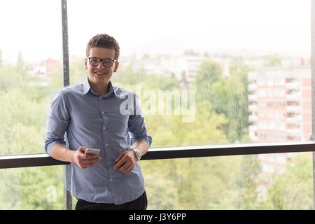 Geschäftsmann mit einem Telefon neben modernen Bürofenster Stockfoto