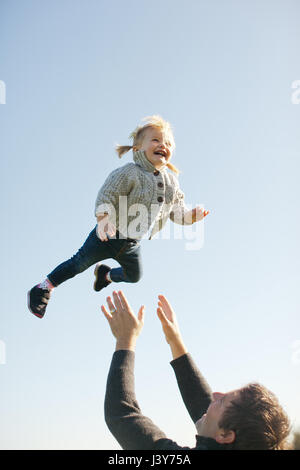 Weiblichen Kleinkind Luft von Vater gegen blauen Himmel geworfen Stockfoto