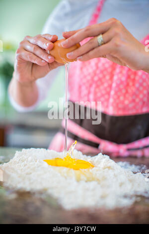 Reife Frau knacken Ei auf Mehl, Mittelteil Stockfoto