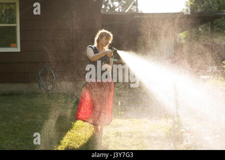 Garten mit Wasser aus Gartenschlauch Spritzen Frau Stockfoto