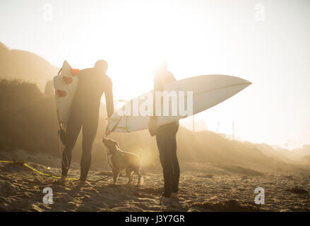 Surfer mit Hund in der Sonne halten Surfbretter am Strand von Malibu, Kalifornien, USA Stockfoto