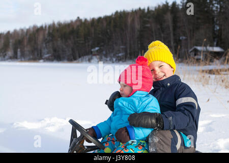 Zwei junge Brüder sitzen auf Schlitten im Schnee bedeckt Landschaft Stockfoto