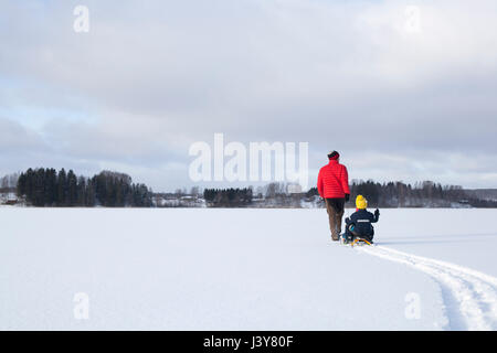 Vater zieht Söhne entlang auf Schlitten im Schnee bedeckte Landschaft, Rückansicht Stockfoto