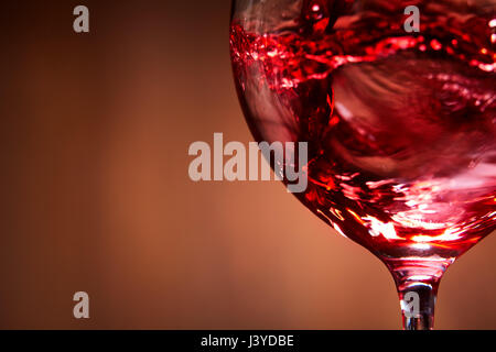 Nahaufnahme von leuchtend rot Wein gegossen in das Weinglas und abstrakte spritzt gegen braunen Hintergrund. Stockfoto