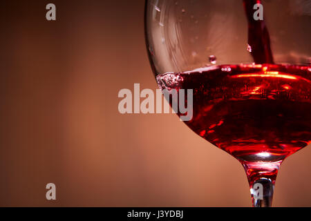 Nahaufnahme von leuchtend rot Wein gegossen in das Weinglas und abstrakte spritzt gegen braunen Hintergrund. Stockfoto