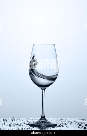 Spritzen transparente Wasserwelle in das Weinglas auf dem Glas gegen hellen Hintergrund stehend. Stockfoto
