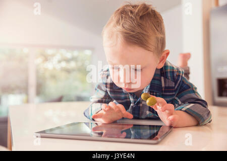 Kleinkind Jungen Blick auf Tablet Oliven in der Küche zu Hause essen Stockfoto