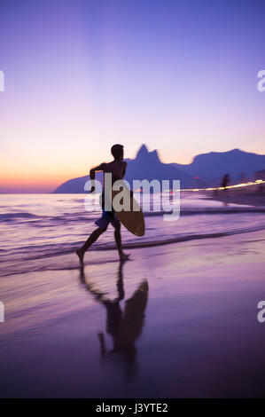 Malerische Aussicht auf den Strand von Ipanema bei Sonnenuntergang mit einer Bewegungsunschärfe Skim Grenze entlang der Küste vor eine Silhouette der beiden Brüder Berg Stockfoto