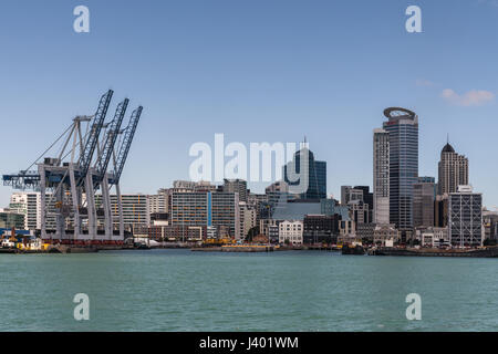 Auckland, Neuseeland - 3. März 2017: Reihe von Containerbrücken am kommerziellen Hafen mit einem Teil der Skyline der Stadt auf der Rückseite unter blauem Himmel und hinter greeni Stockfoto