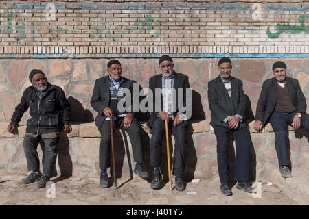 Ältere Männer sitzen auf der Bank vor lokalen Imanzadeh, Rooieen (Ruine), ein traditionelles Dorf, Nord-Chorasan, IRAN - 04.01.2017. Ortszeit Stockfoto