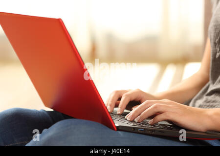 Hände eines einzigen Mädchens eine rote Laptop sitzen auf dem Boden des Wohnzimmers zu Hause mit einem Fenster und warmes Licht im Hintergrund e-Mail eintippen Stockfoto