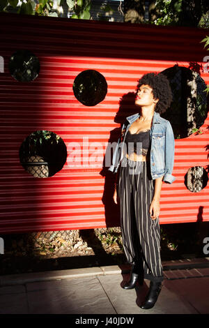Junge weibliche Mode-Blogger mit Augen geschlossen von sonnenbeschienenen Zaun, New York, USA Stockfoto