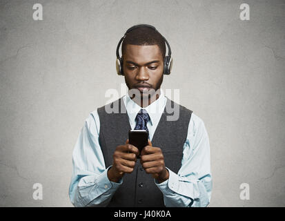 Closeup Portrait ernst konzentrierte sich auf der Suche, Geschäftsmann mit Kopfhörern lesen Nachrichten, Sms auf smart Phone, mobile isolierte graue Wand Hintergrund halten. Stockfoto