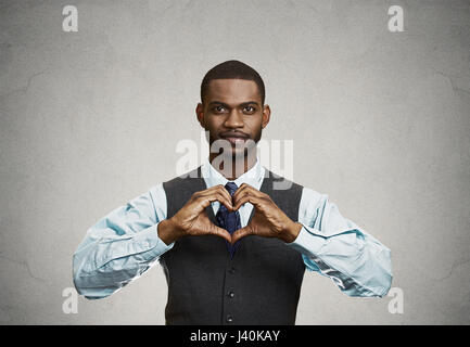 Closeup Portrait hübscher junger Geschäftsmann lächelnd lässt das Herz mit Fingern, Händen, vereinzelte graue Wand Hintergrund. Positive Emotionen, fac Stockfoto
