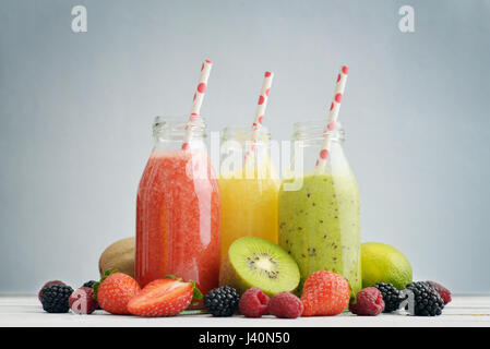 Frucht-Smoothies in Retro-Flaschen mit Erdbeeren, Kiwi, Brombeere, Himbeere und Orange auf blauem Hintergrund. Stockfoto