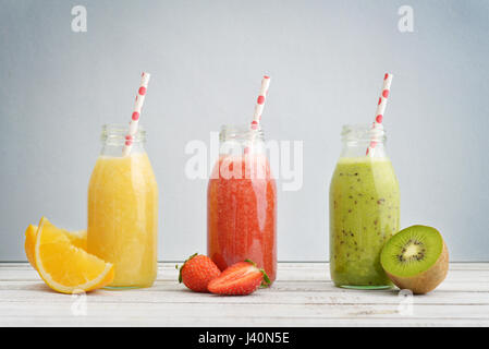 Frucht-Smoothies in Retro-Flaschen mit Erdbeeren, Kiwi und Orange auf blauem Hintergrund. Stockfoto