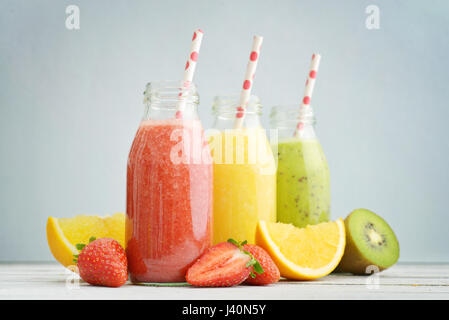 Frucht-Smoothies in Retro-Flaschen mit Erdbeeren, Kiwi und Orange auf blauem Hintergrund. Stockfoto