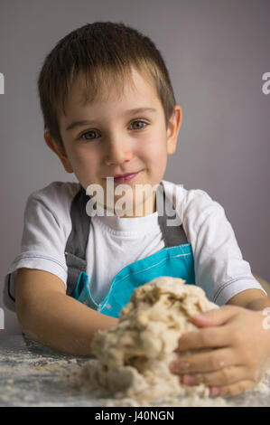 Little Boy ist rohe Pizzateig zu kneten und lächelnd Stockfoto