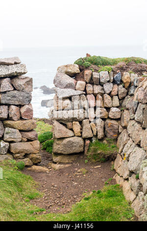 Ein Squeeze-Stil in einer Trockensteinmauer gebaut aus Granitblöcken in verschiedenen Größen und Farben bei Cape Cornwall, Cornwall, England, UK Stockfoto