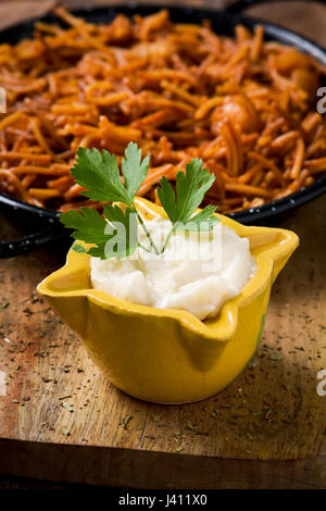 Nahaufnahme von einem gelben Mörser mit Aioli-Sauce und eine spanische Fideua, eine typische Nudeln Auflauf mit Meeresfrüchten in einer Paellapfanne auf einem rustikalen Holztisch Stockfoto