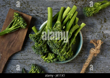 High-Angle Shot einige Stämme von Broccolini in eine grüne Keramikplatte platziert auf einem grauen rustikalen Holztisch Stockfoto