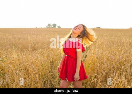 Wunderschöne romantische Mädchen im Freien. Schönes Modell in kurzen roten Kleid im Feld. Lange Haare im Wind wehen. Hintergrundbeleuchtung, warme Farbtöne. Stockfoto