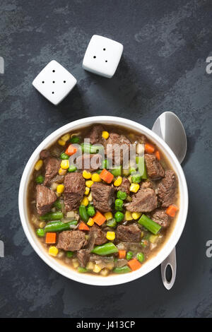 Rindfleisch-Eintopf oder Suppe mit bunten Sommer-Gemüse (Erbsen, Karotten, Mais, grüne Bohnen, Zwiebel) in Schüssel Stockfoto