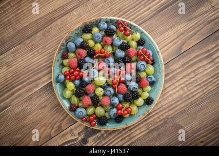 Volle Schüssel mit saftigen Reifen Sommerbeeren auf hölzernen Hintergrund Stockfoto