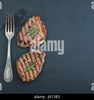 Gegrilltes Steak mit Gabel auf schwarzem Schiefer Hintergrund, Ansicht von oben Stockfoto