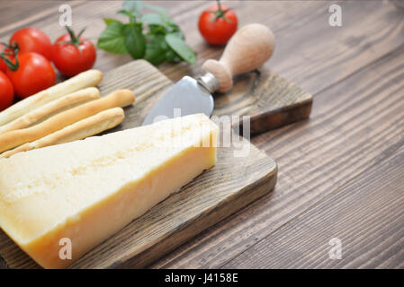 Parmesan-Käse auf Schneidebrett mit Basilikum und Messer auf Holz Hintergrund Stockfoto