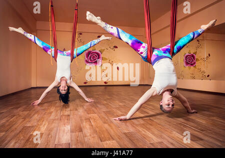 Zwei junge Frau beim Antigravity Yoga invertiert Position am Wellness-Studio mit Rose an der Wand Stockfoto