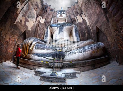 Frau im roten t-Shirt stehen in der Nähe von riesigen Buddha-Statue Phra Achana in Wat Si Chum in Sukhothai Historical Park, Thailand anrufen Stockfoto