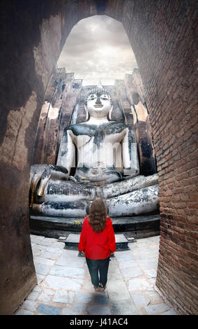 Frau im roten t-Shirt stehen in der Nähe von riesigen Buddha-Statue Phra Achana in Wat Si Chum in Sukhothai Historical Park, Thailand anrufen Stockfoto