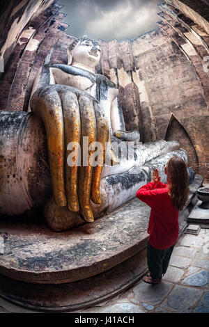 Frau im roten t-Shirt stehen in der Nähe von riesigen Buddha-Statue Phra Achana in Wat Si Chum in Sukhothai Historical Park, Thailand anrufen Stockfoto