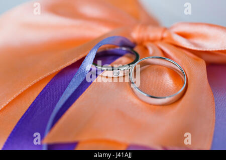 Trauringe auf einem Korallen satin Kissen. einen großen Bogen. Zubehör Hochzeit Closeup. selektiven Fokus Stockfoto