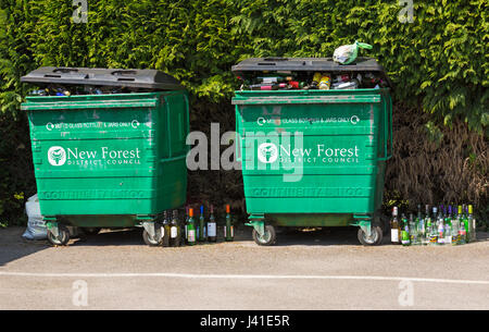 Recycling-Behälter für gemischte Glasflaschen und Gläser nur durch New Forest District Council - überquellenden Mülltonnen mit Flaschen auf dem Boden an der Seite Stockfoto