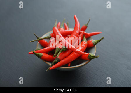 Rote Chilischoten in Schüssel auf schwarzem Schiefer Hintergrund Stockfoto