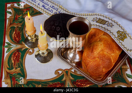 Schabbat-Kerzen im Glas Leuchter i unscharfer Hintergrund überdachte Challah Brot in silbernen Tablett auf weißes Tischtuch. Stockfoto